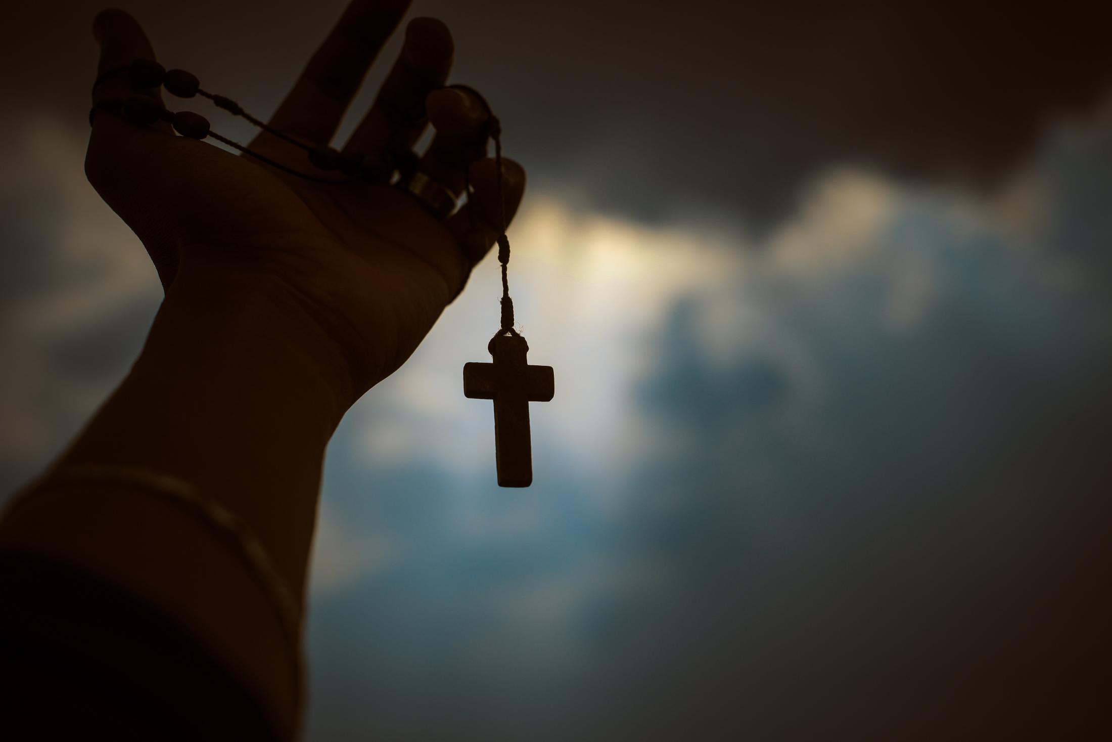 Silhouette of hand holding a rosary in front of a dark sky