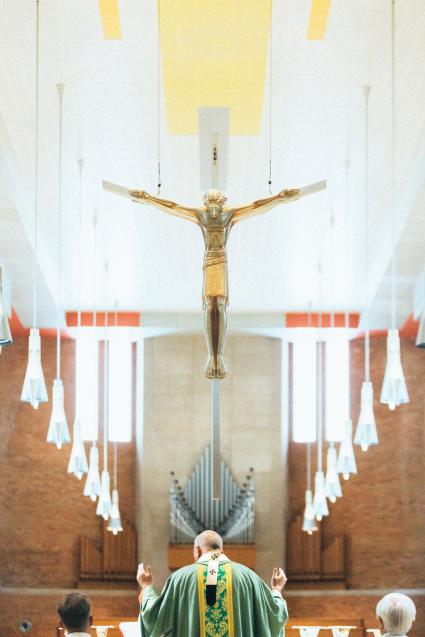 Catholic priest standing at altar with crucifix hanging above and his back to camera