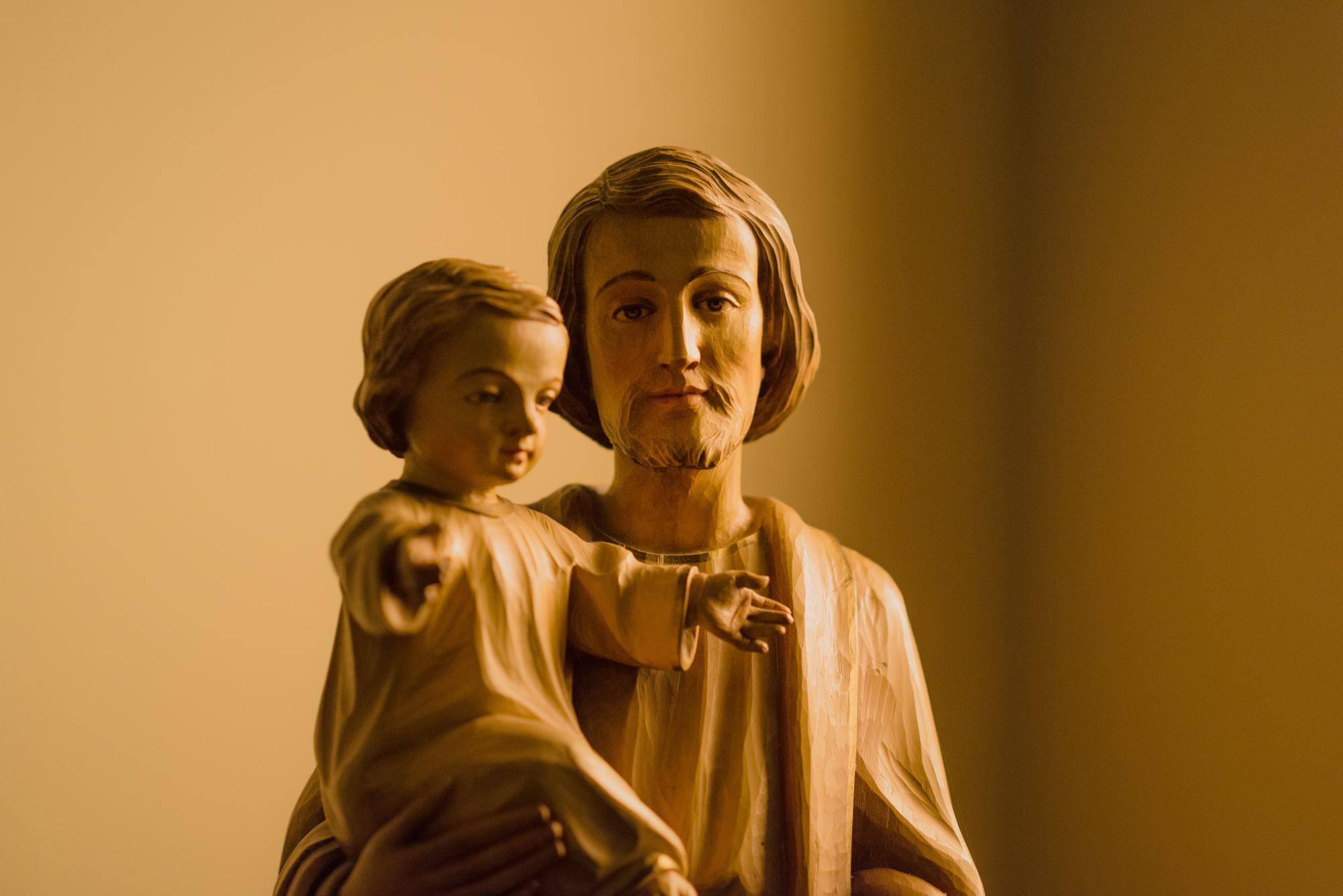 Statue of St. Joseph, appearing to look at the camera, as he holds the infant Jesus.