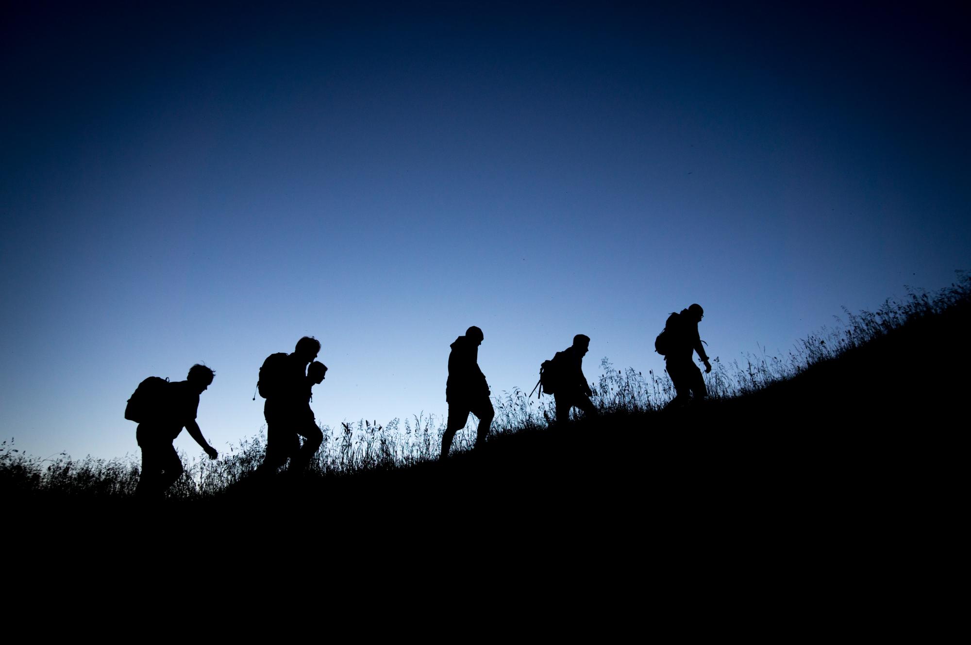 Silhouette of people climbing up a hill