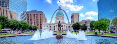 fountain in front of Missouri state house with statue of man. Gateway arch framing capitol building in the background