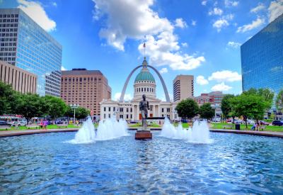 fountain in front of Missouri state house with statue of man. Gateway arch framing capitol building in the background