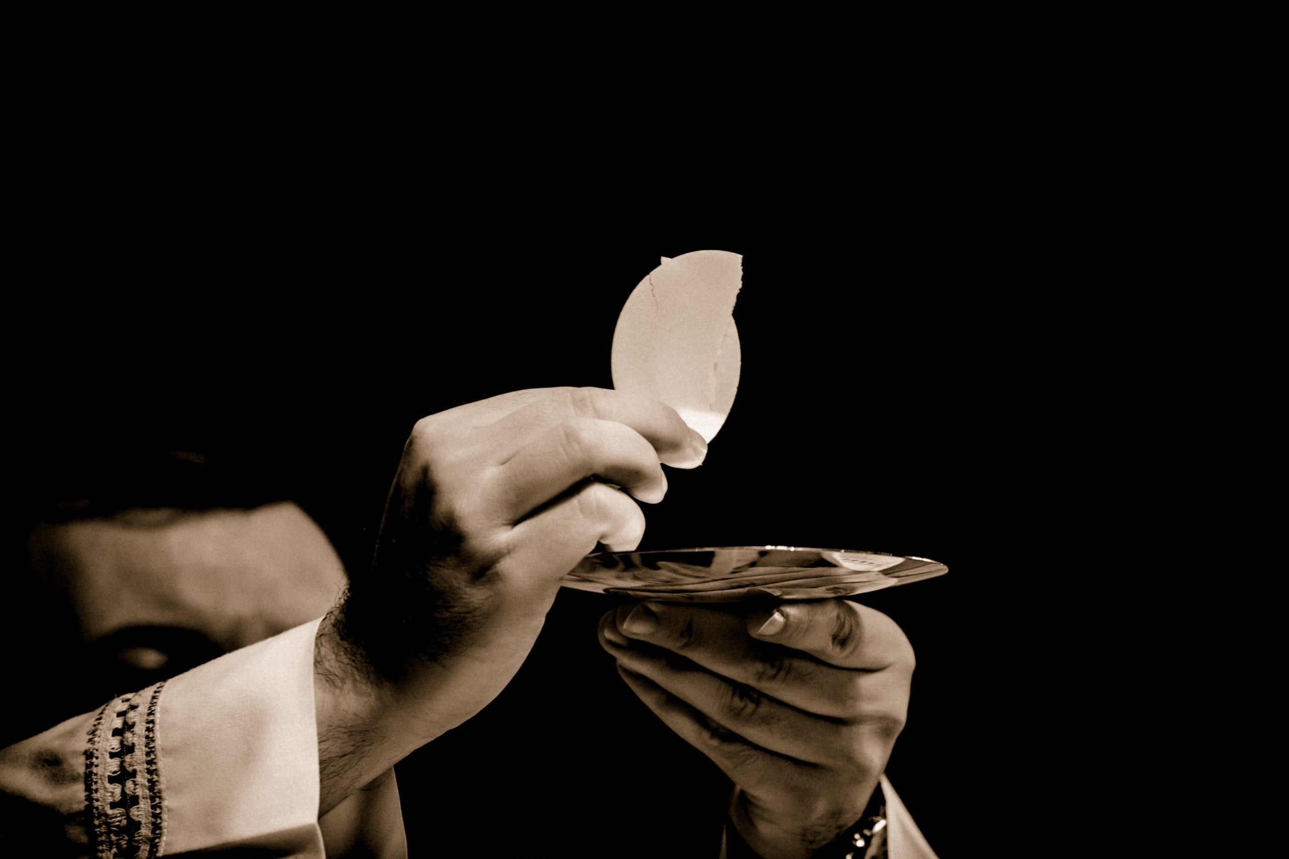 Image: hands holding the Body of Christ with black background